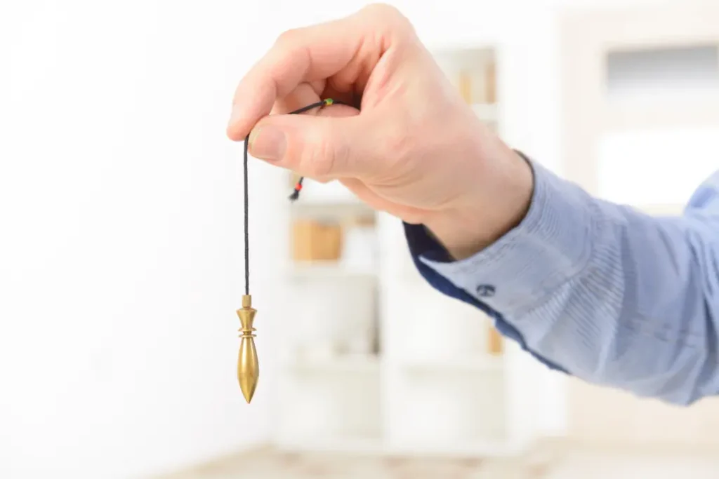 Una mano sostiene un péndulo dorado - curso de radiestesia